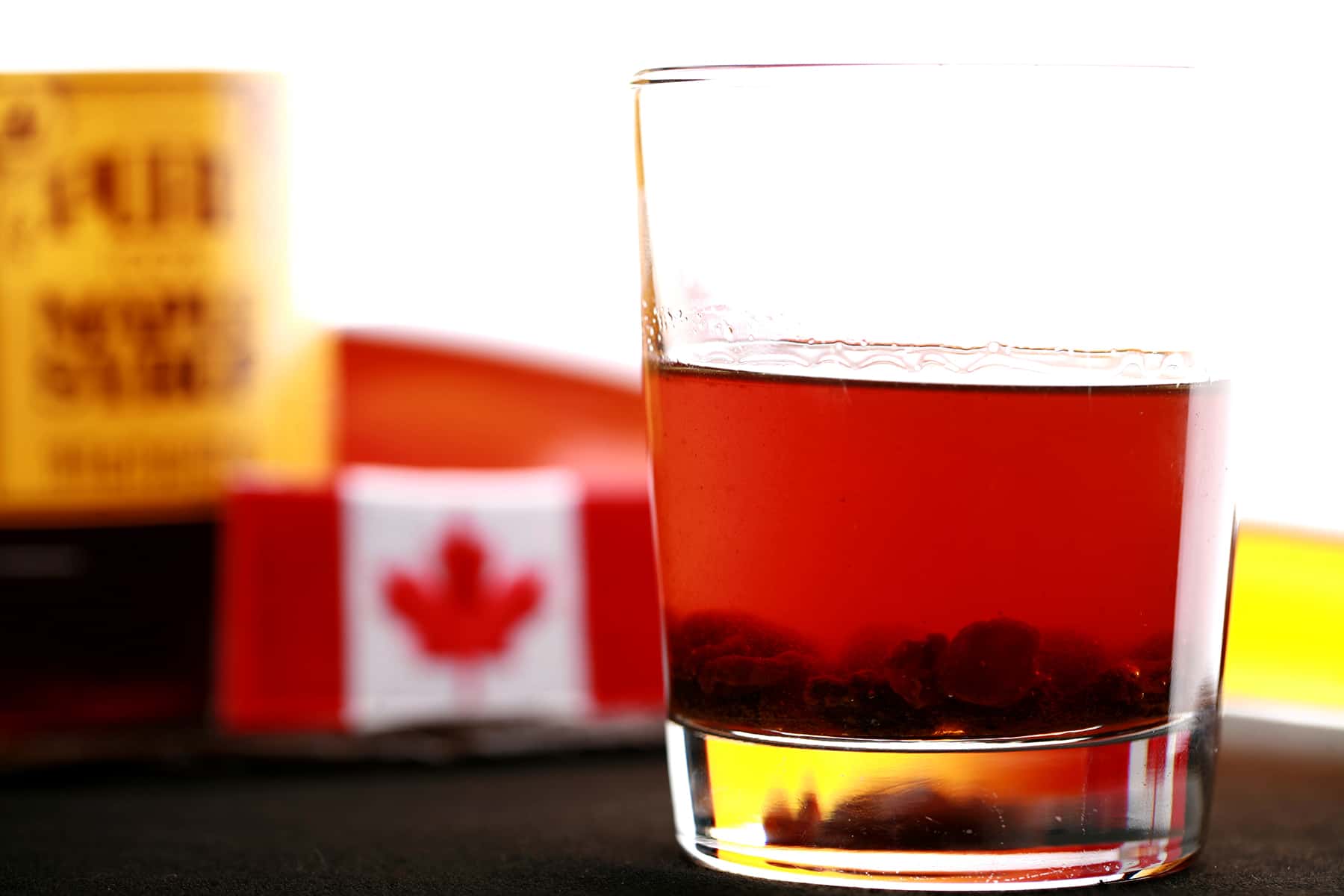 A glass of maple buttertart liqueur in front of a Canadian flag.