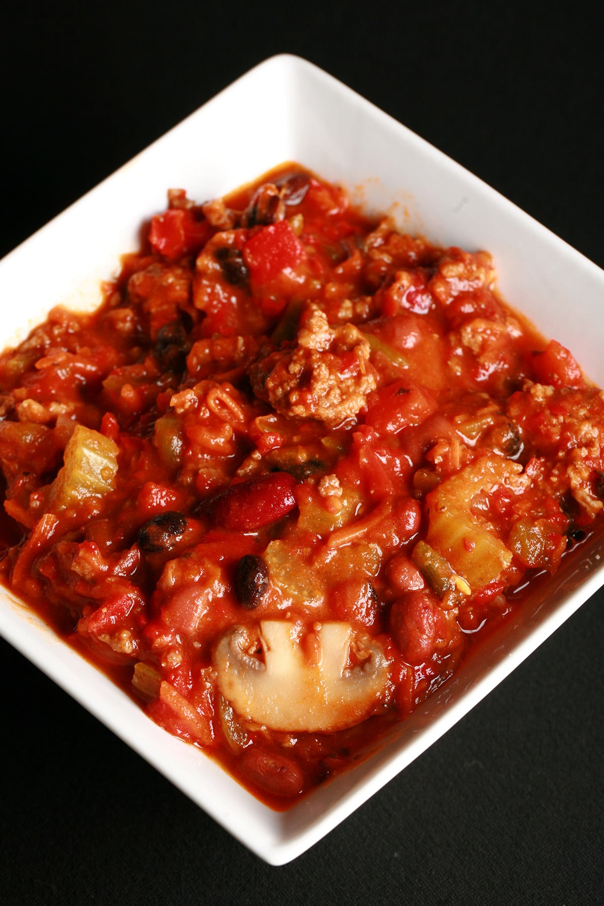Close up photo of a bowl of chili. Kidney beans, ground beef, mushrooms, celery, and red peppers are visible.