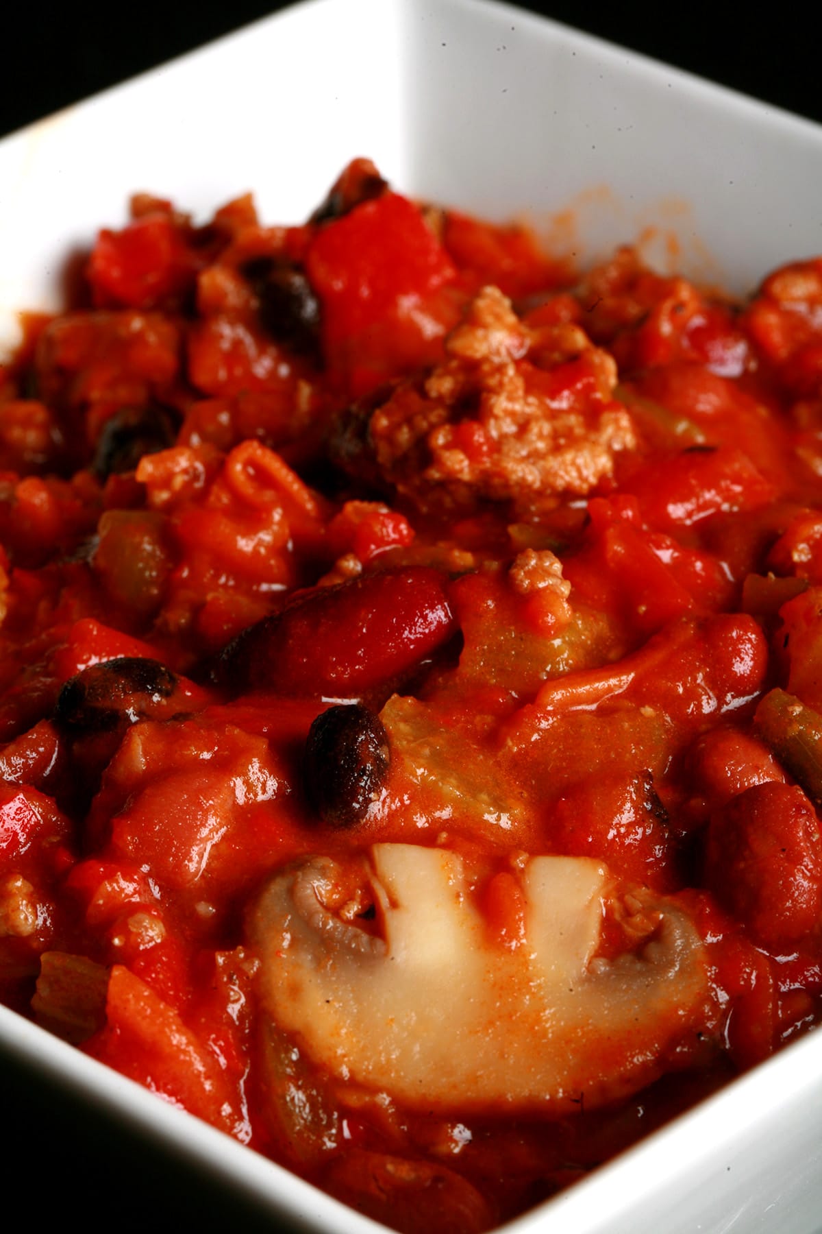 Close up photo of a bowl of chili. Kidney beans, ground beef, mushrooms, celery, and red peppers are visible.