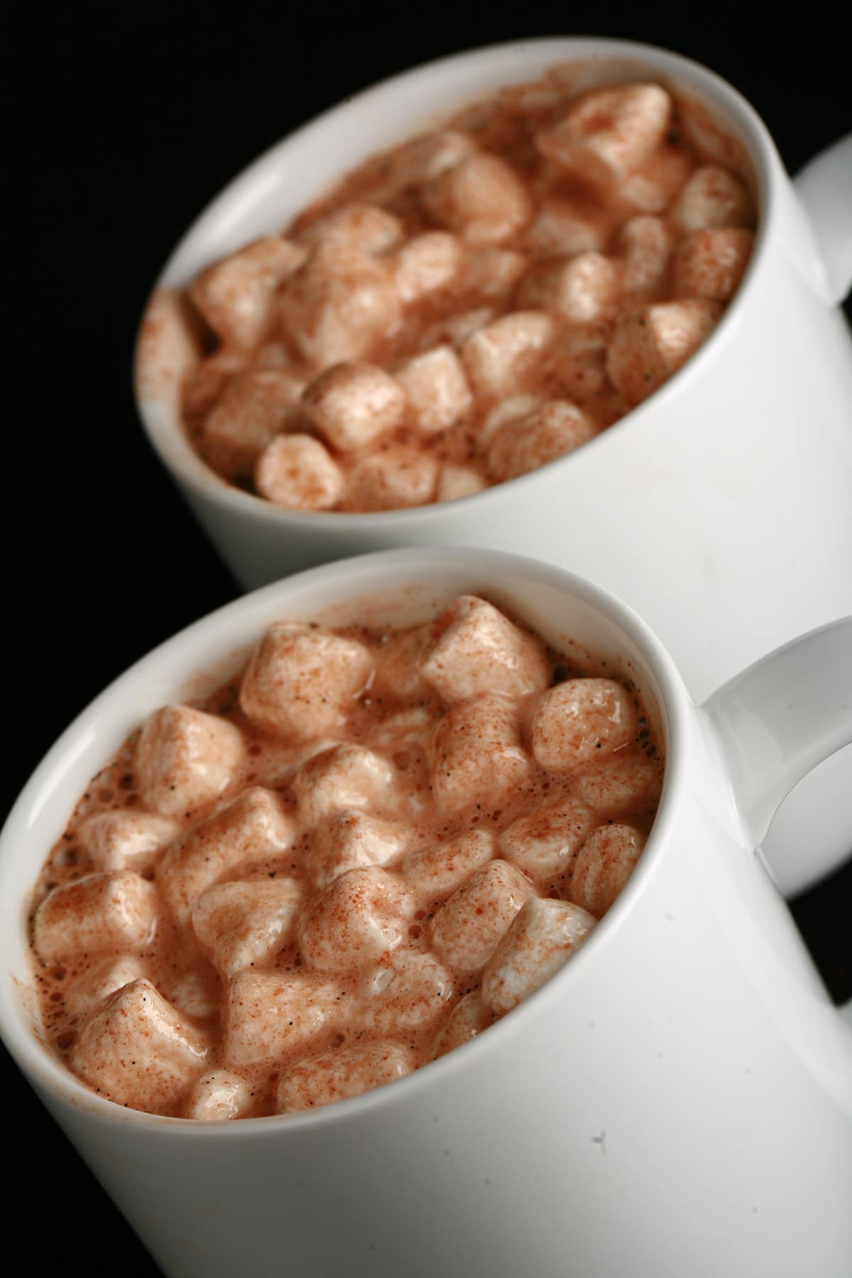 2 white mugs of grownup hot chocolate, with mini marshmallows and alcohol.