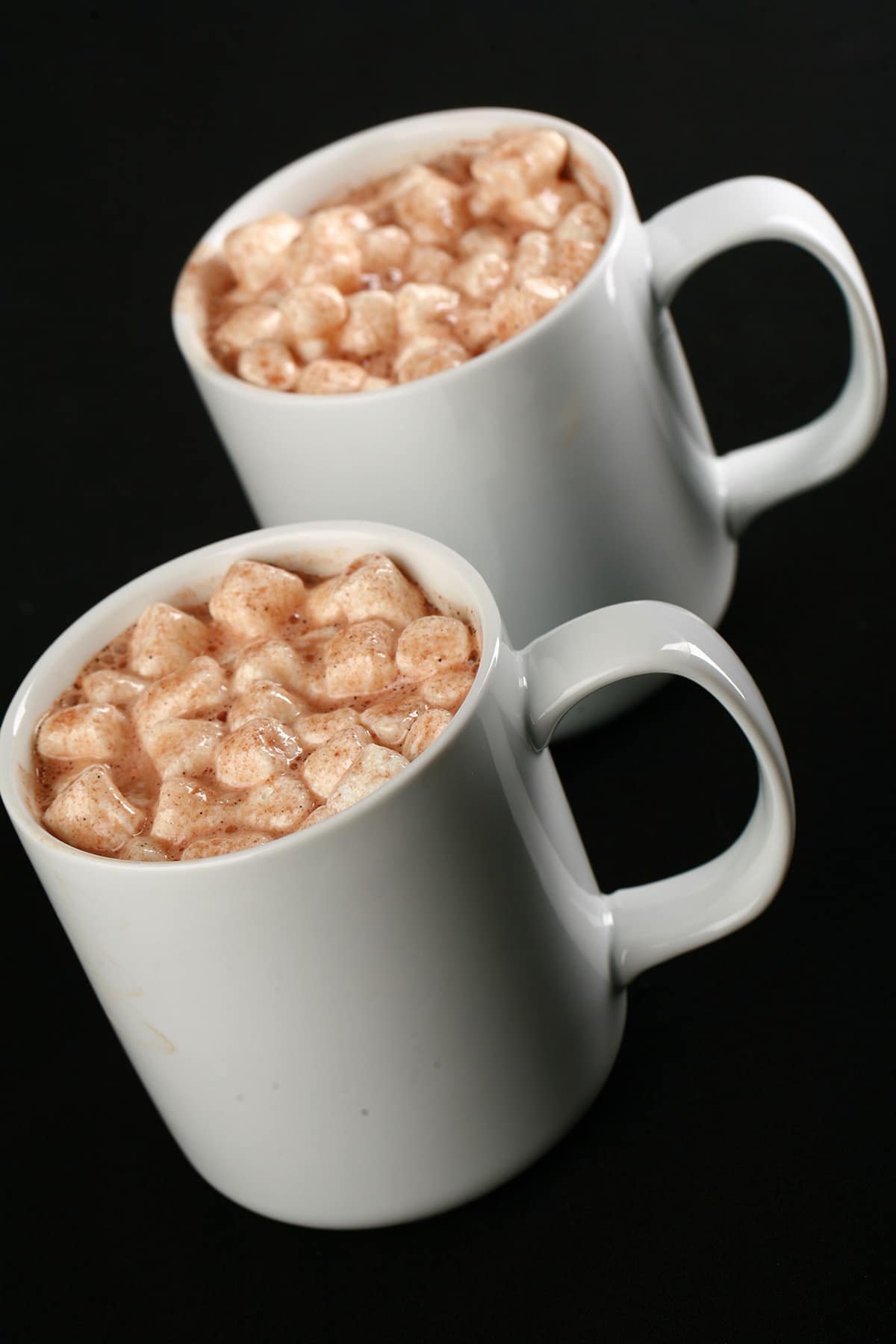 2 white mugs of grownup hot cocoa, with mini marshmallows and alcohol.