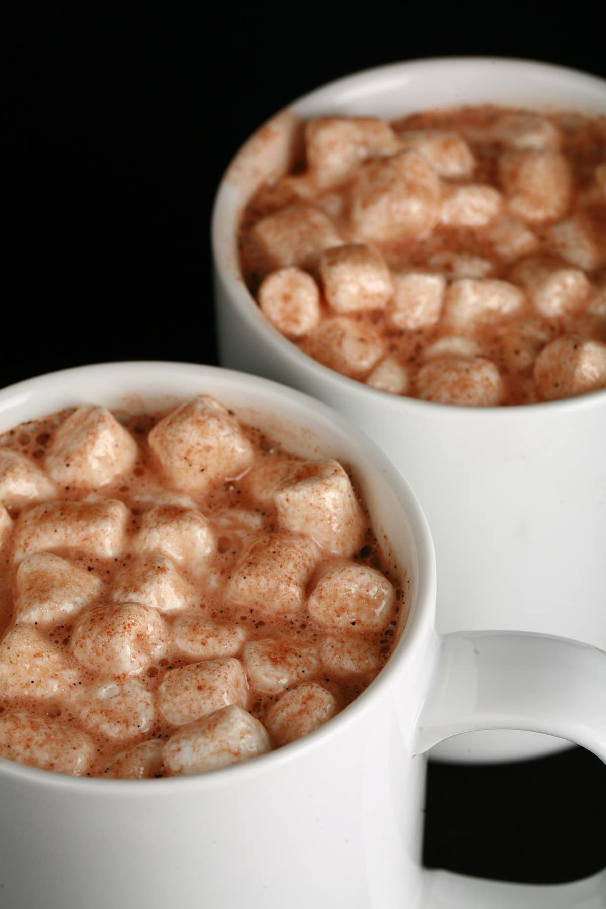 2 white mugs of grownup hot cocoa, with mini marshmallows and alcohol.