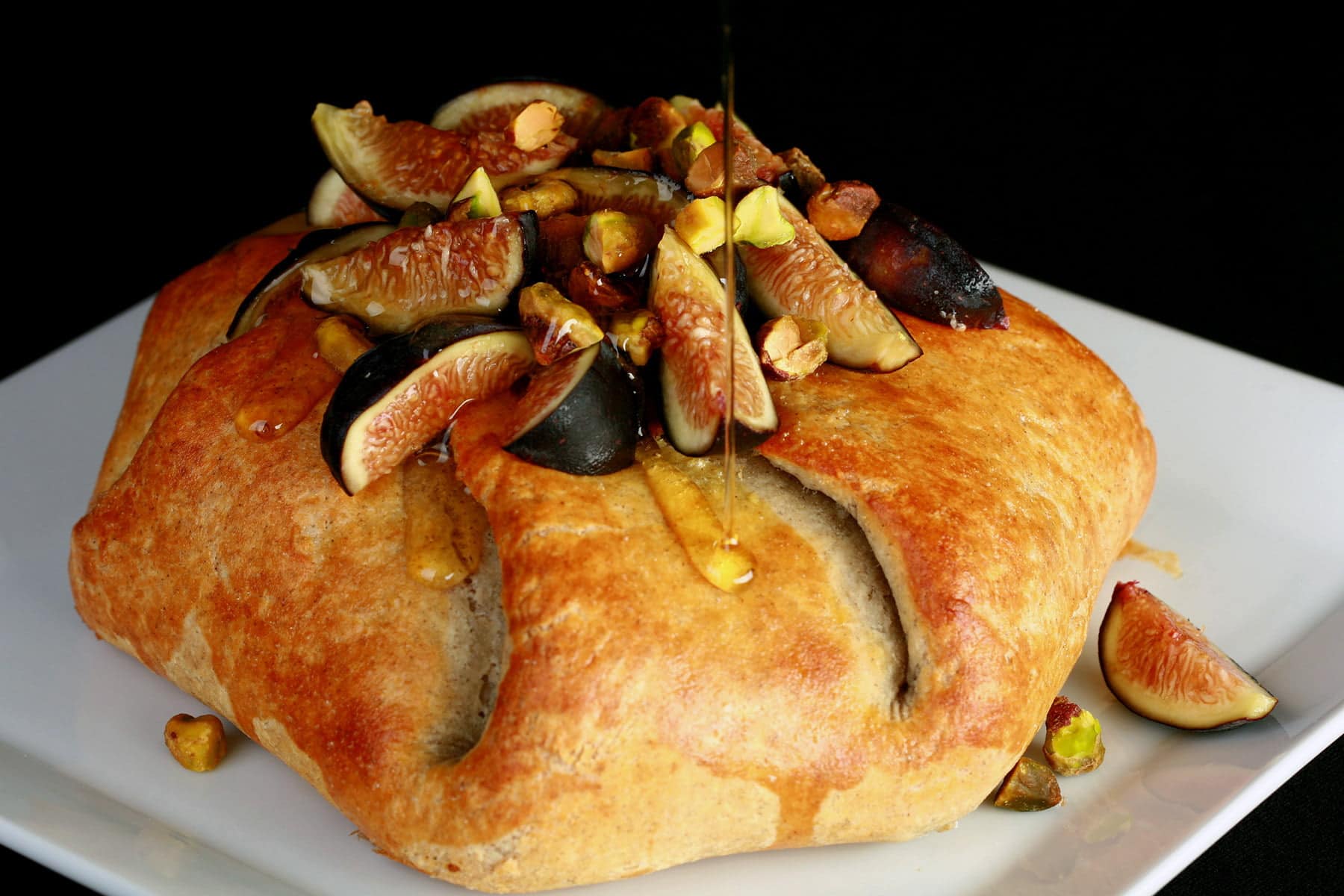 Sliced figs, pistachio, and honey top a round, gathered, golden brown pastry.