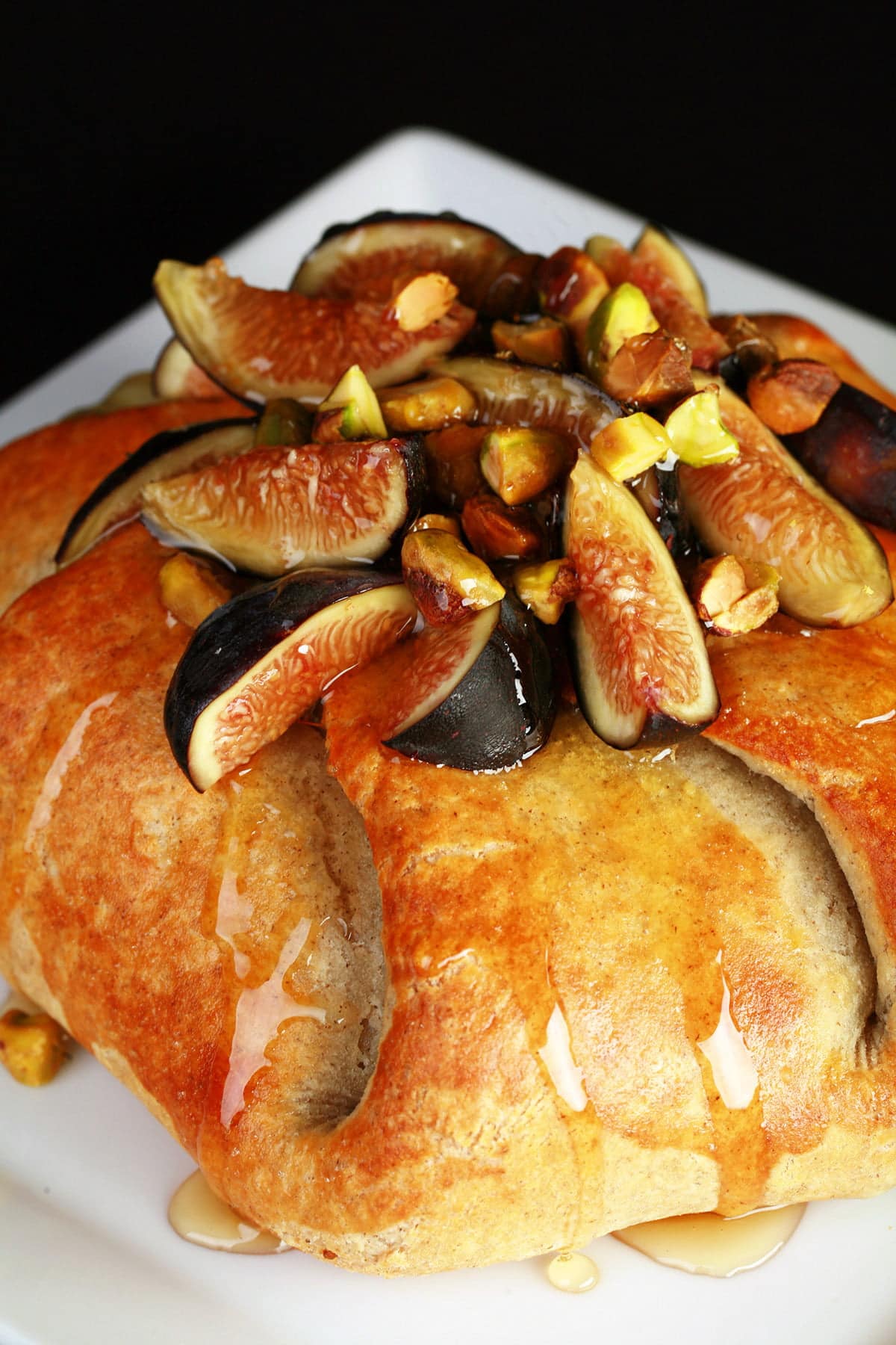 Sliced figs, pistachio, and honey top a round, gathered, golden brown pastry.