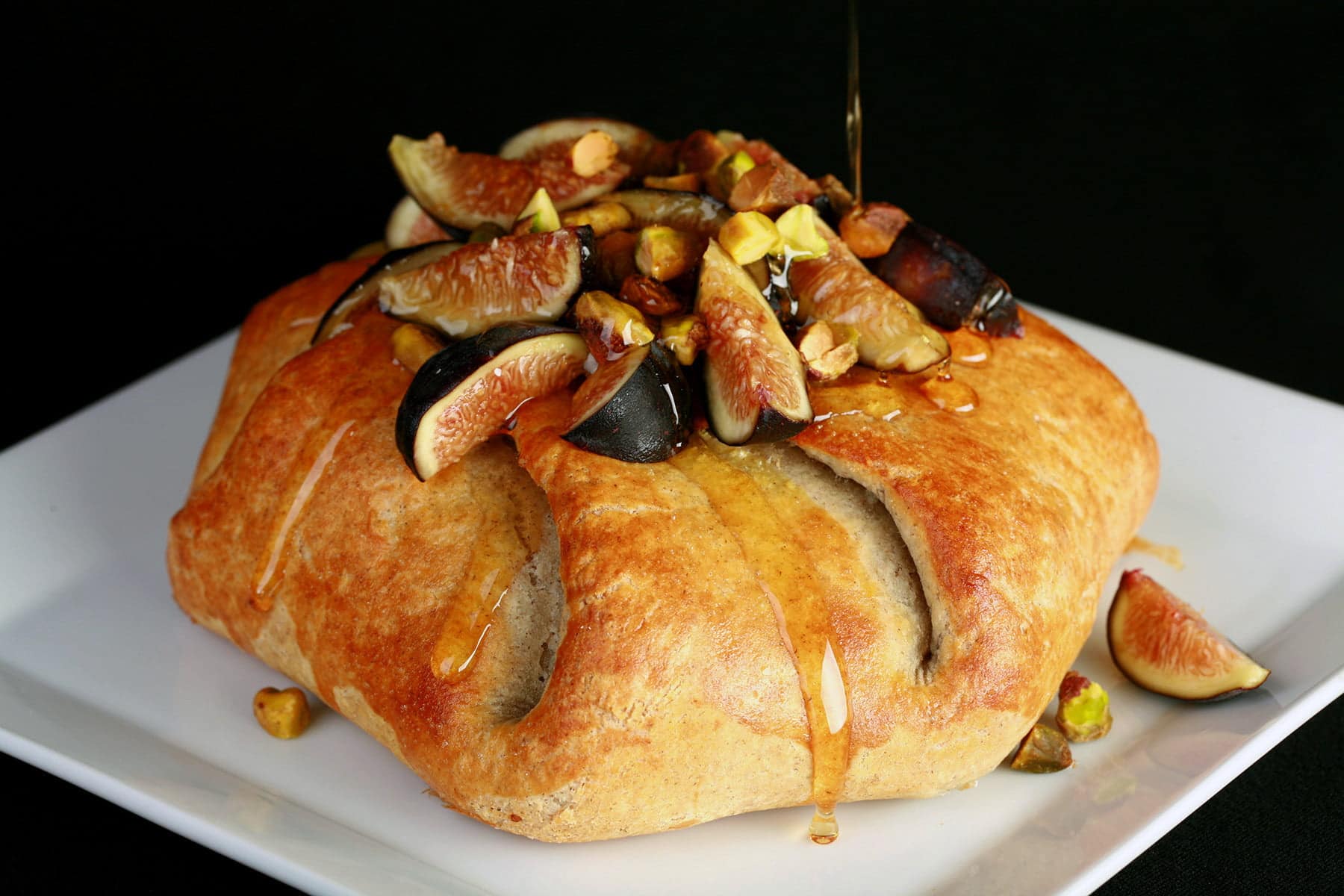 Sliced figs, pistachio, and honey top a round, gathered, golden brown pastry.