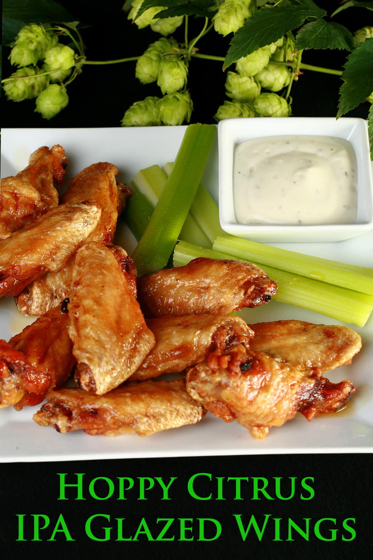A plate of deep fried, Hoppy Citrus IPA Glazed Wings. They;re on a plate with celery sticks and a little bowl of ranch sauce, and the plate is surrounded by fresh hop bines.