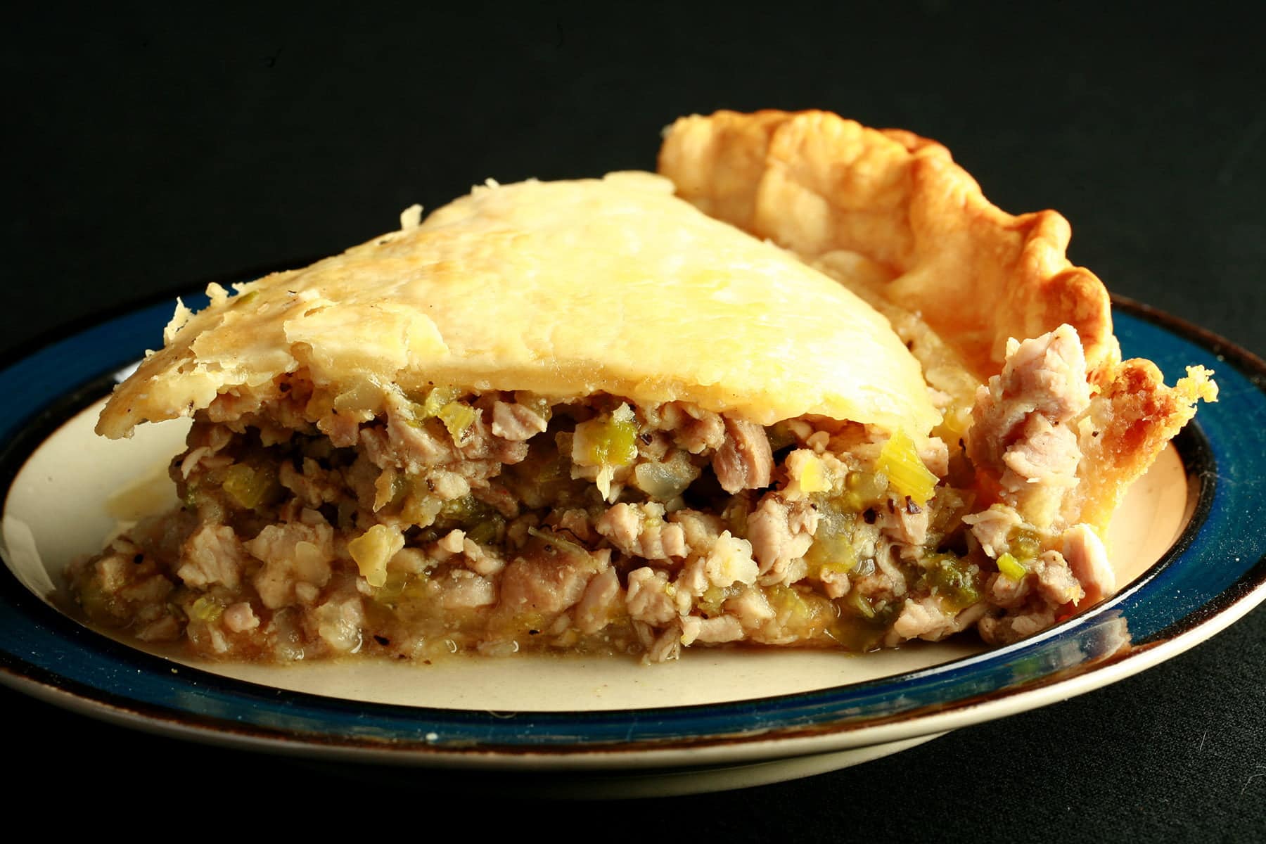 A slice of savory alligator pie, on a small white plate. The filling shows chunks of meat and vegetables, like celery.