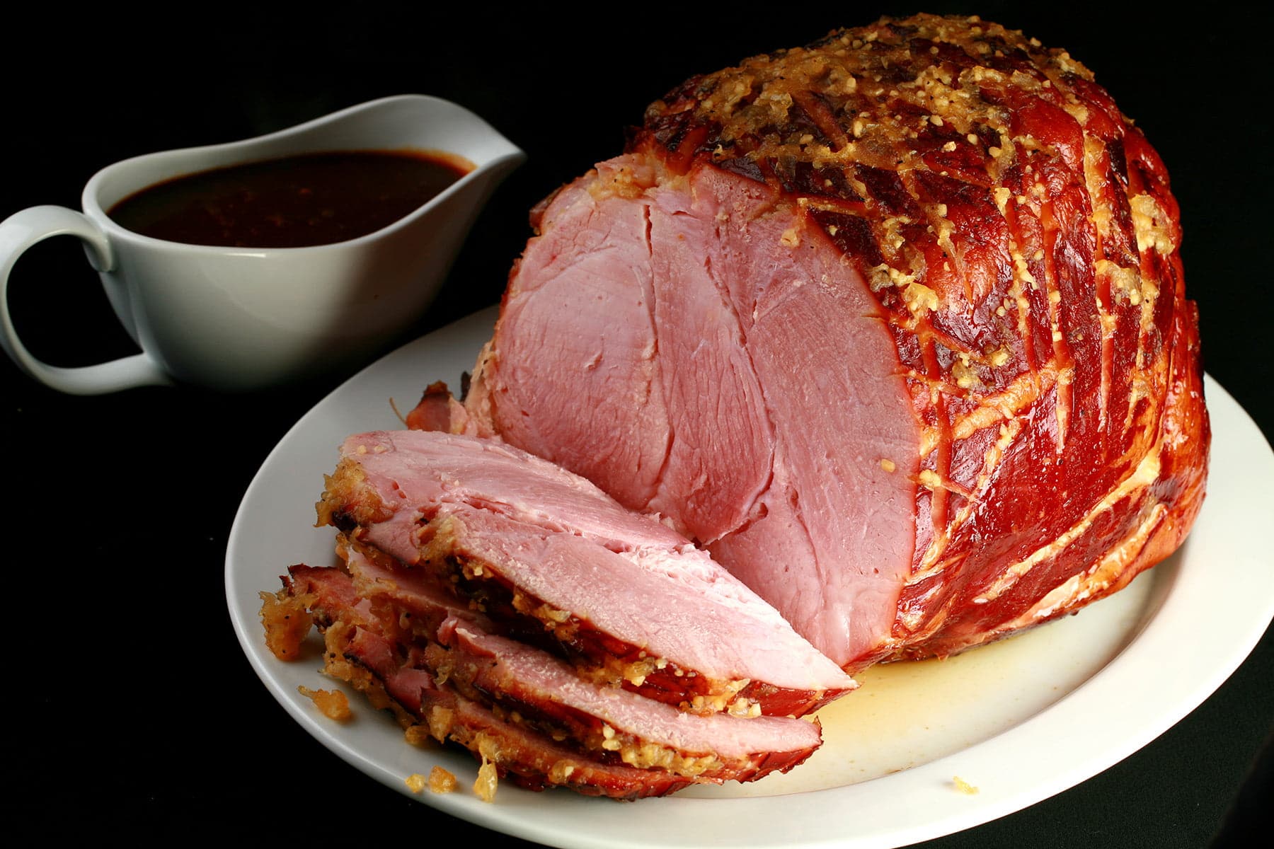 A large ham on a white platter. There are several generous slices of ham in the foreground.
