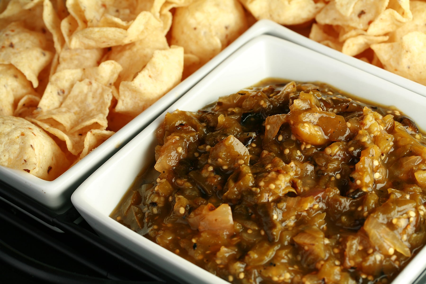 A large square bowl of roasted salsa verde, surrounded by white corn chips.