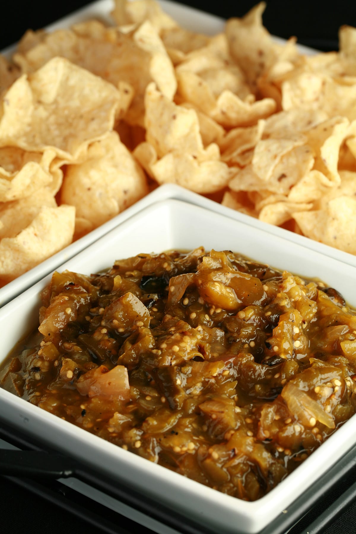 A large square bowl of roasted salsa verde, surrounded by white corn chips.