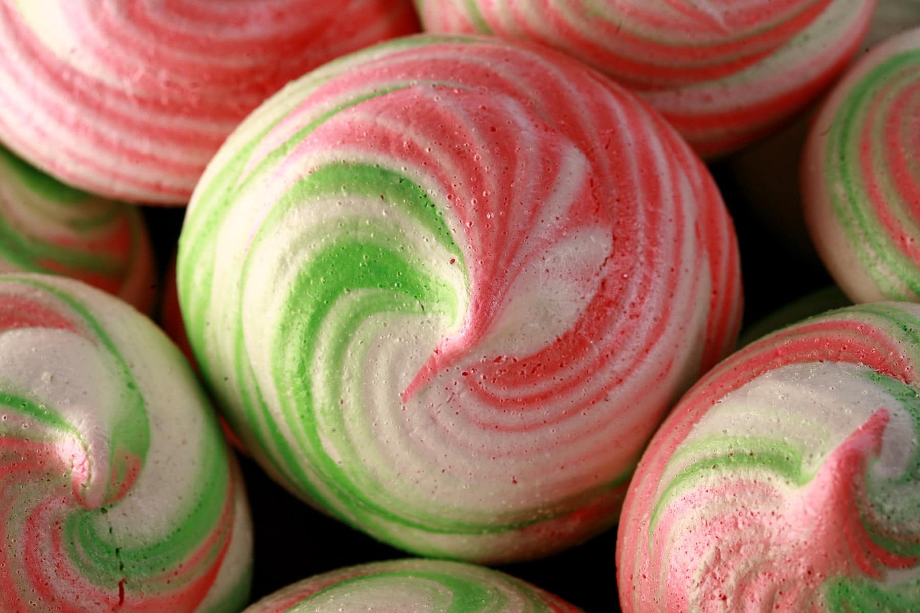 A small plate is piled with pretty, tri-coloured peppermint swirl meringue cookies in pink, green, and white.