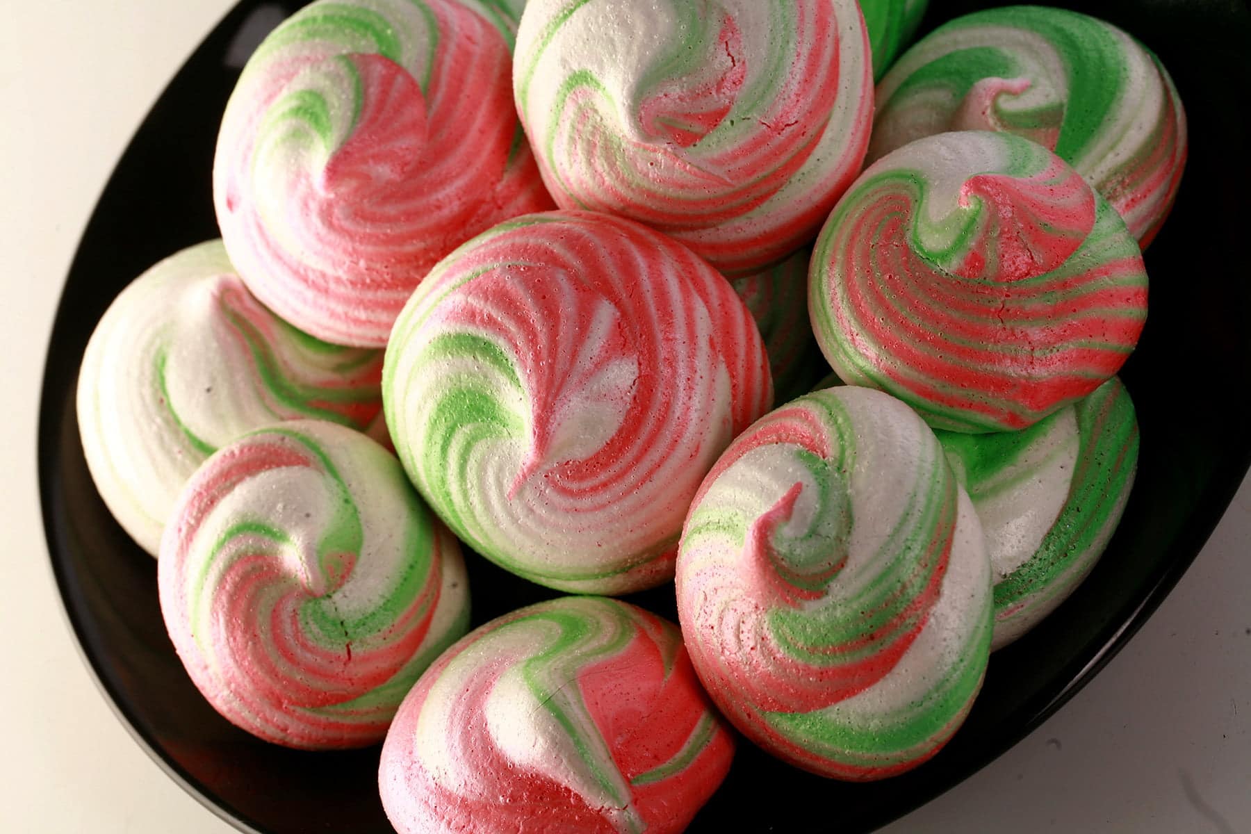 A plate of swirled meringue cookies in shades of pink, white, and green.