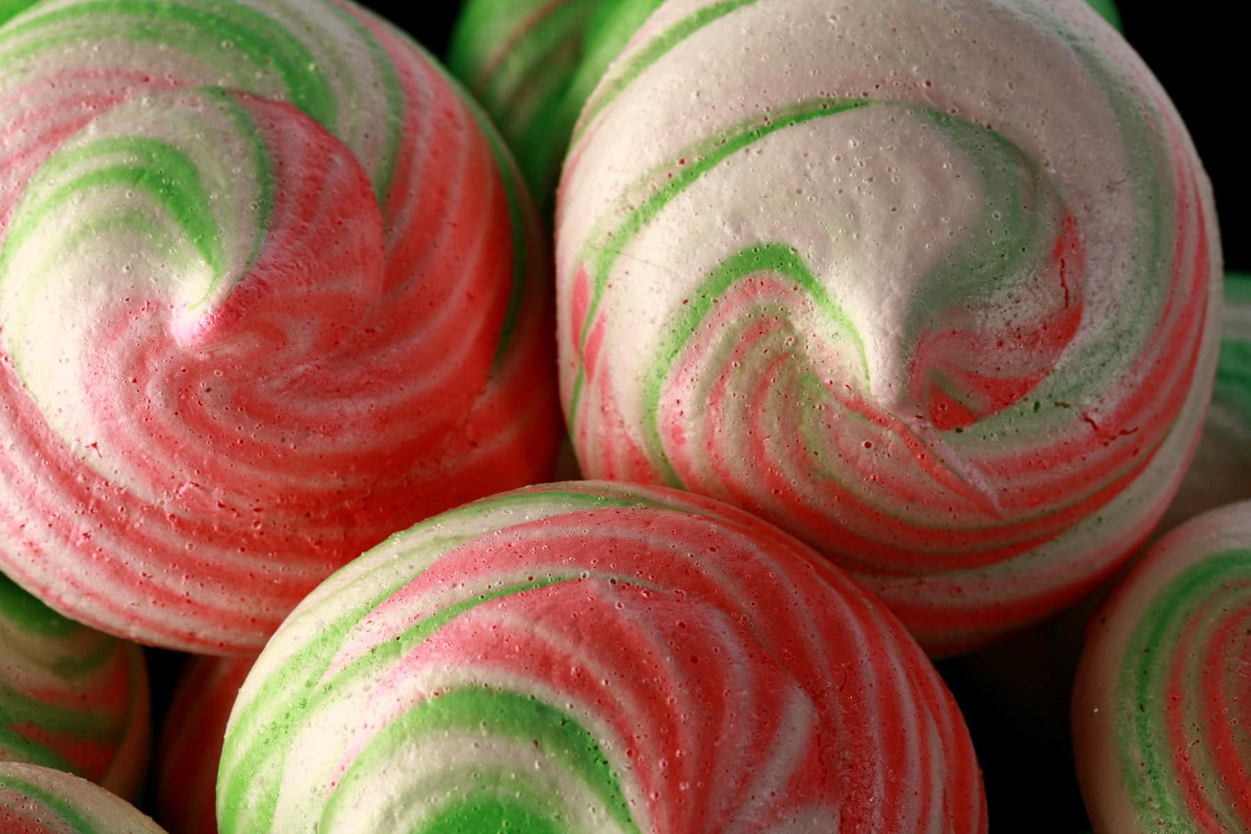 A small plate is piled with pretty meringue cookies in swirls of pink, green, and white.