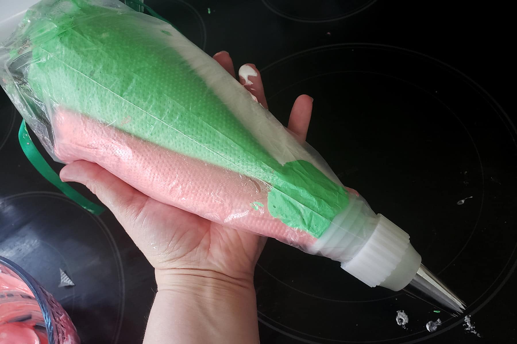 A hand holds a pastry bag filled with 3 other pastry bags, holding pink, white, and green meringues.