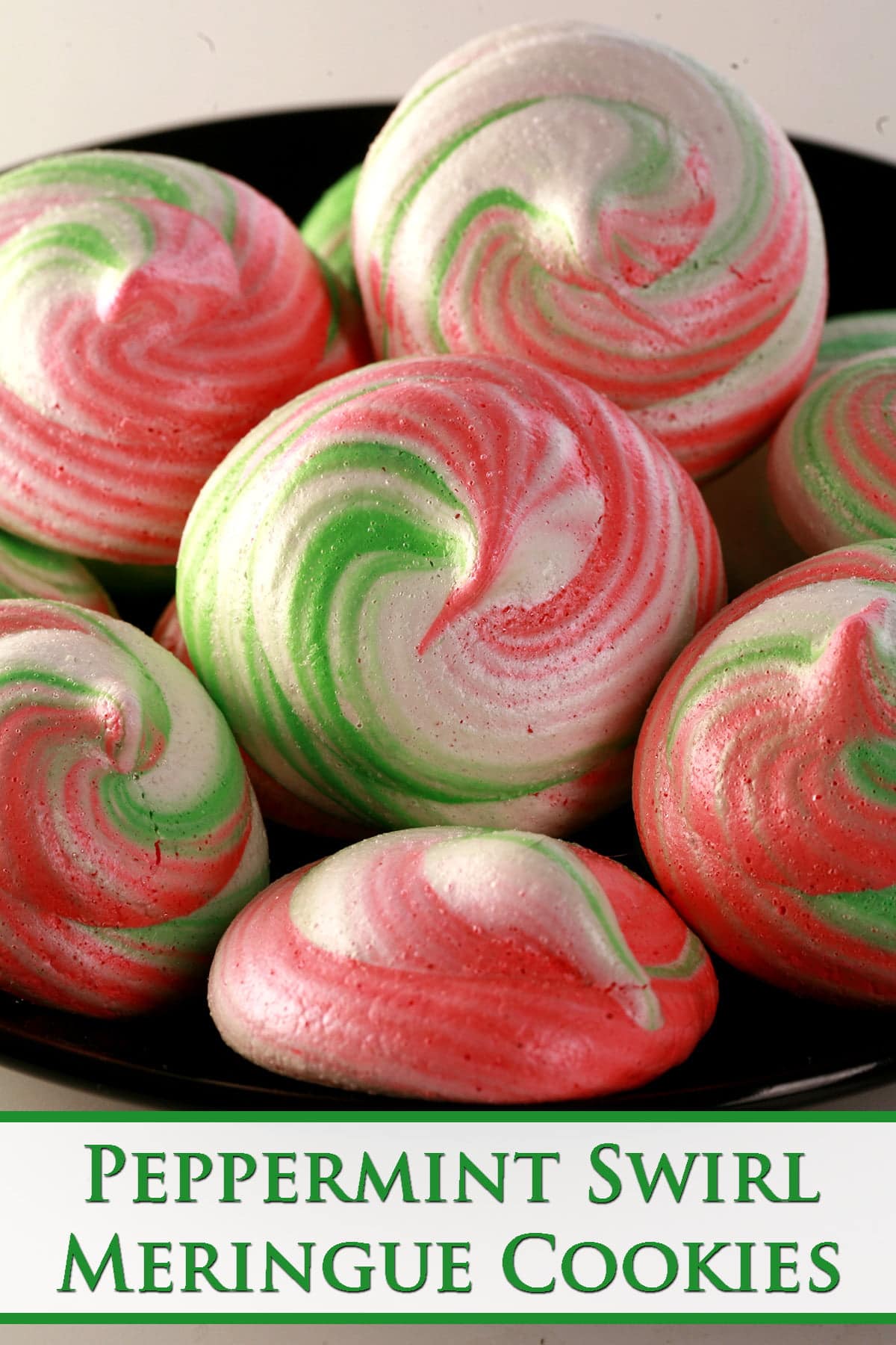 A small plate is piled with pretty, tri-coloured peppermint swirl meringue cookies in pink, green, and white.