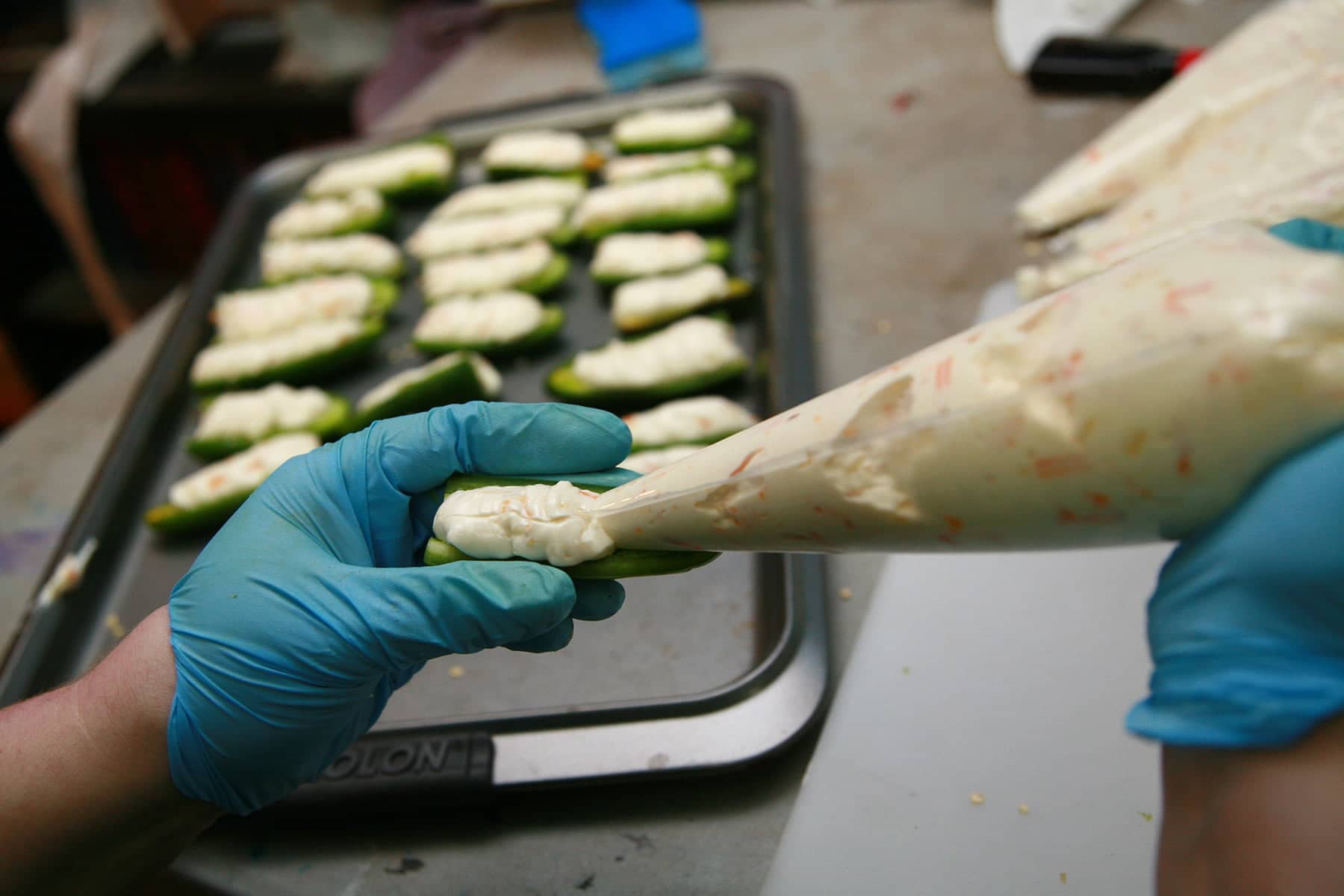 Gloved hands use a pastry bag to pipe cheese mixture into a halved jalapeno pepper.