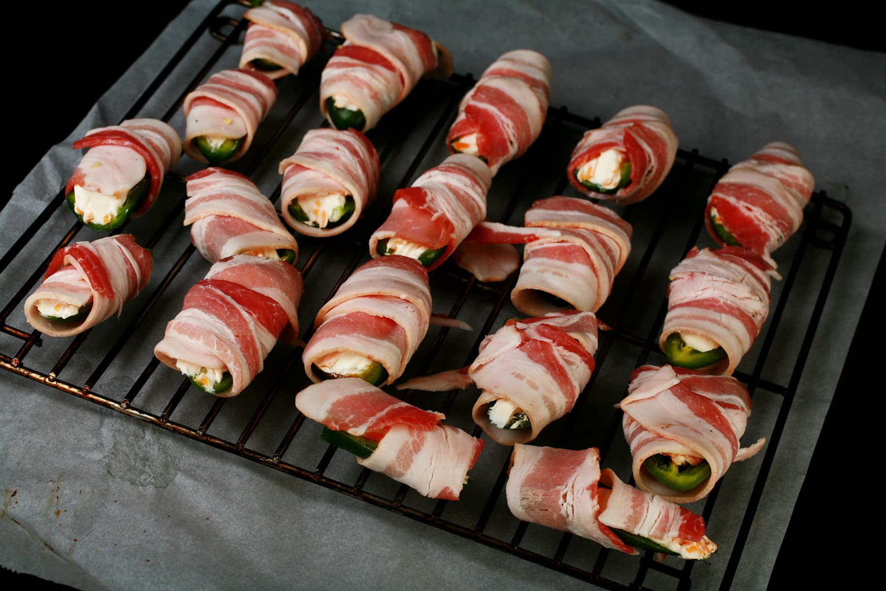 Bacon wrapped cheese stuffed jalapeno pepper halves are arranged on a grill.