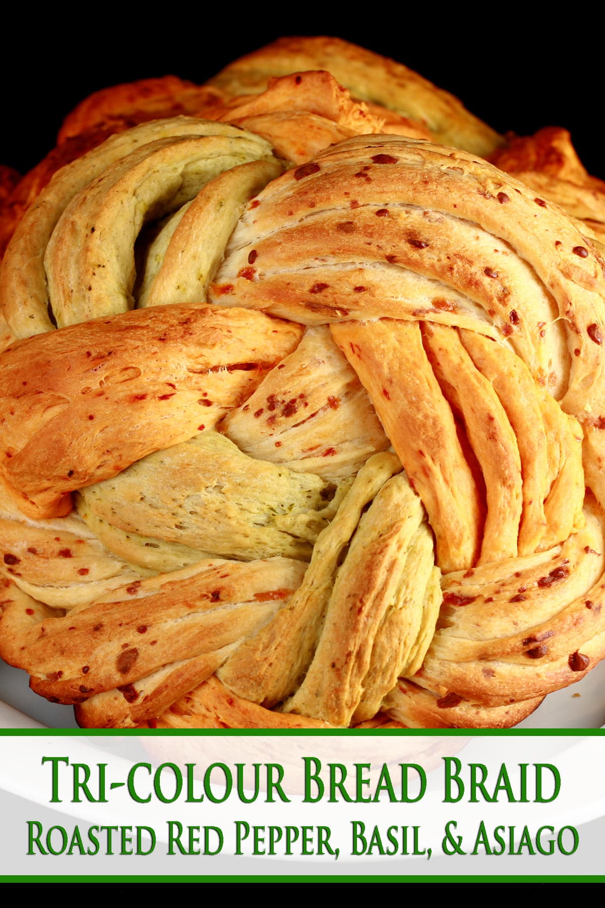 A large round loaf of a tri-colour braid bread. The breads are green/basil, tan/asiago, and red/roasted red pepper.