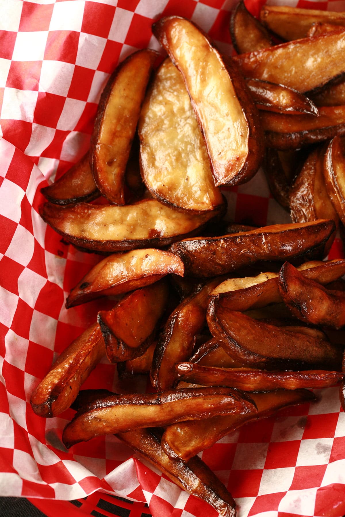 A red basket lined with red and white checkerboard paper holds a batch of smoked french fries that have been cooked in an air fryer.