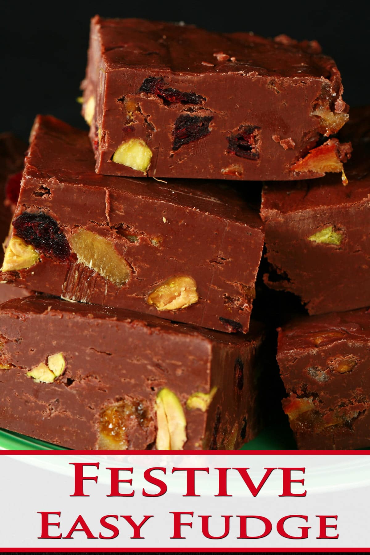 A green plate with a pile of chocolate fudge on it. Each square of fudge is studded with nuts, dried cranberries, candied orange peel, and candied ginger.