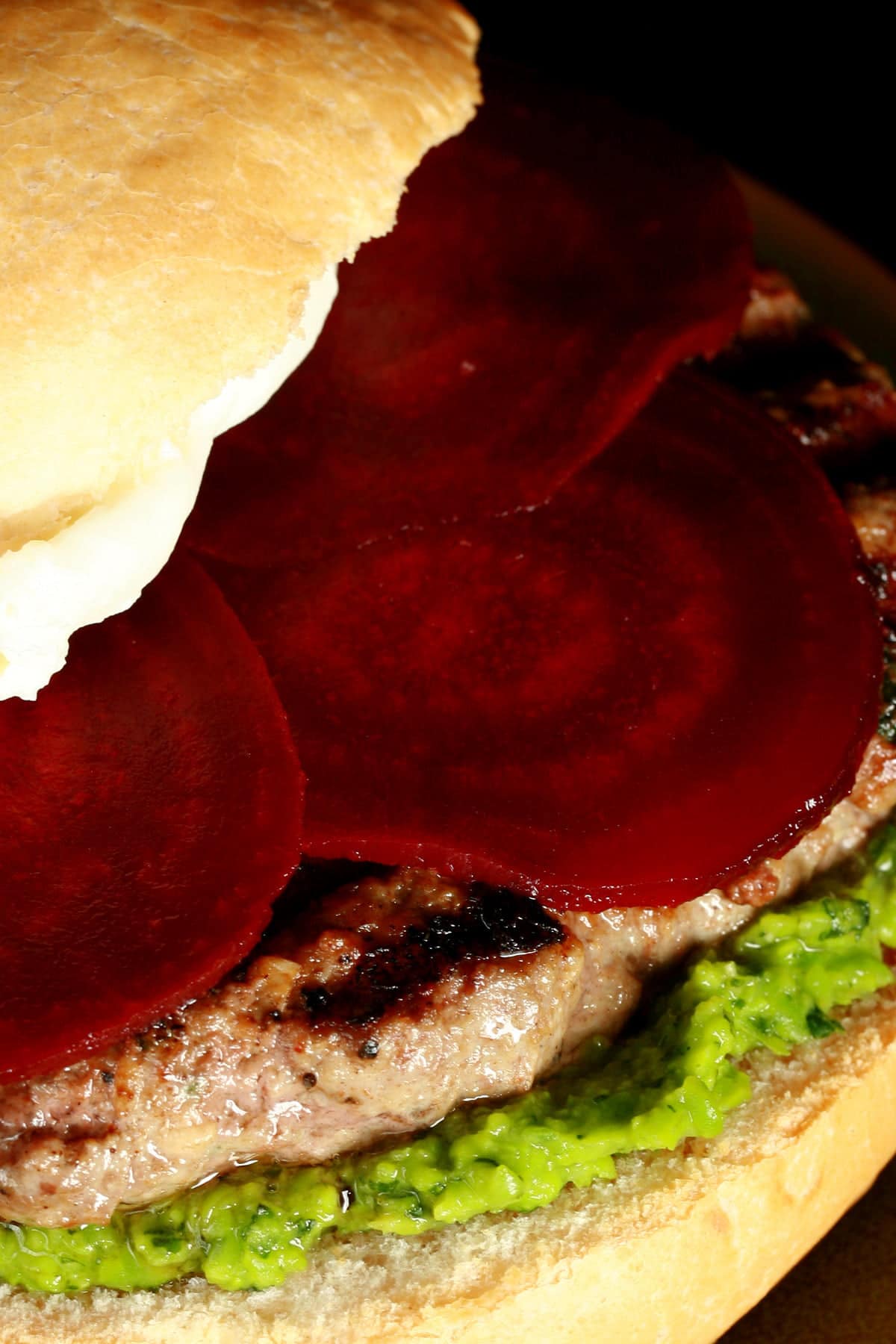 Close up view of a burger with a green spread, a goat cheese spread, and beet slices on it.