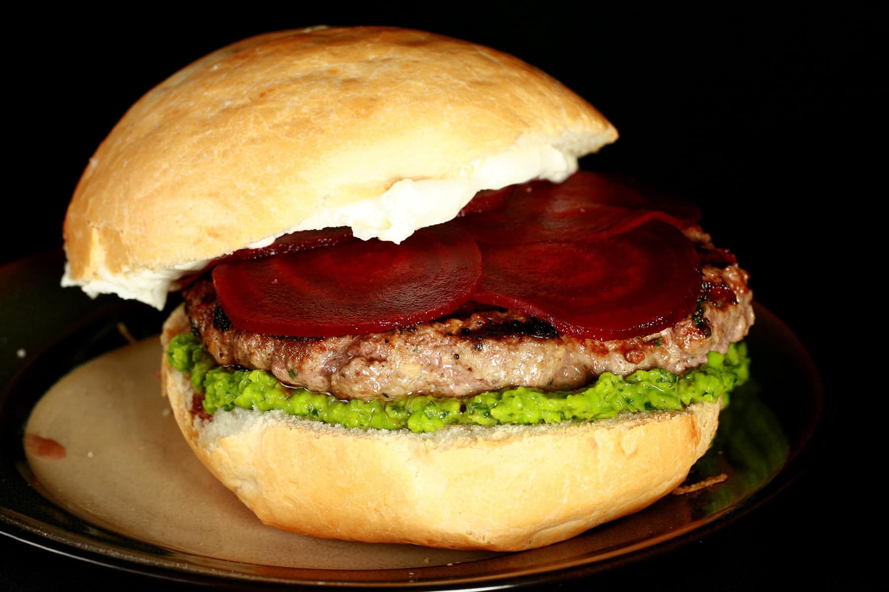Close up view of a moroccan spiced lamb burger with a green spread, a goat cheese spread, and beet slices on it.