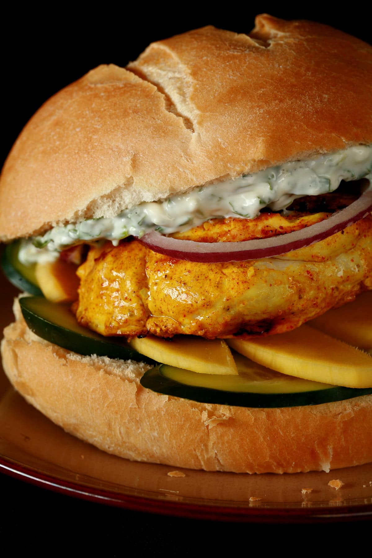 A Tandoori Spiced Chicken Burger: Tandoori Marinated chicken breast with cucumbers, mango, red onions, and a cilantro mint mayo.
