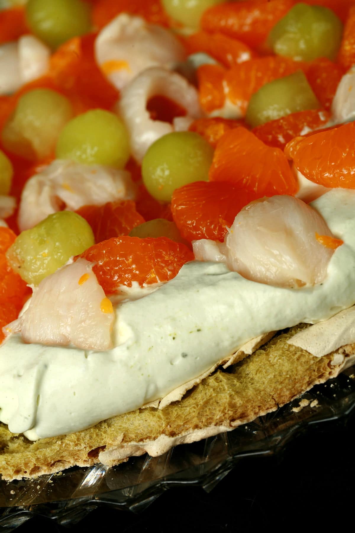 A Green Tea Pavlova with Mandarin orange segments, lychee, and honeydew melon on top.