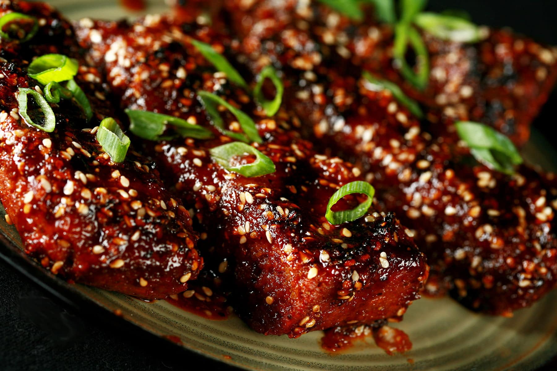 Close up photo of a plate of vegetarian boneless ribs. They're covered in a red-brown sauce, sesame seeds, and sliced green onion.