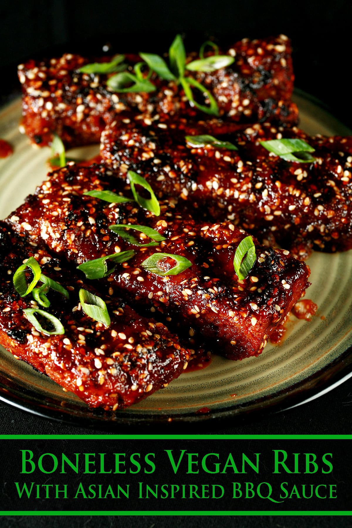 Close up photo of a plate of boneless ribs. They're covered in a red-brown sauce, sesame seeds, and sliced green onion.