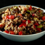 A bowl of wild rice and edamame salad. Wild rice, edamame, and red peppers are all visible.
