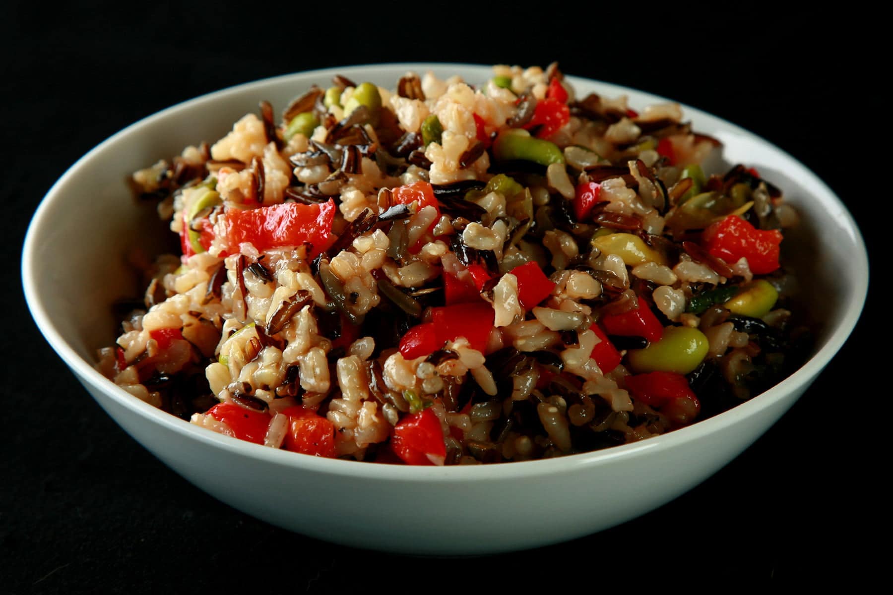 A bowl of wild rice and edamame salad. Wild rice, edamame, and red peppers are all visible.