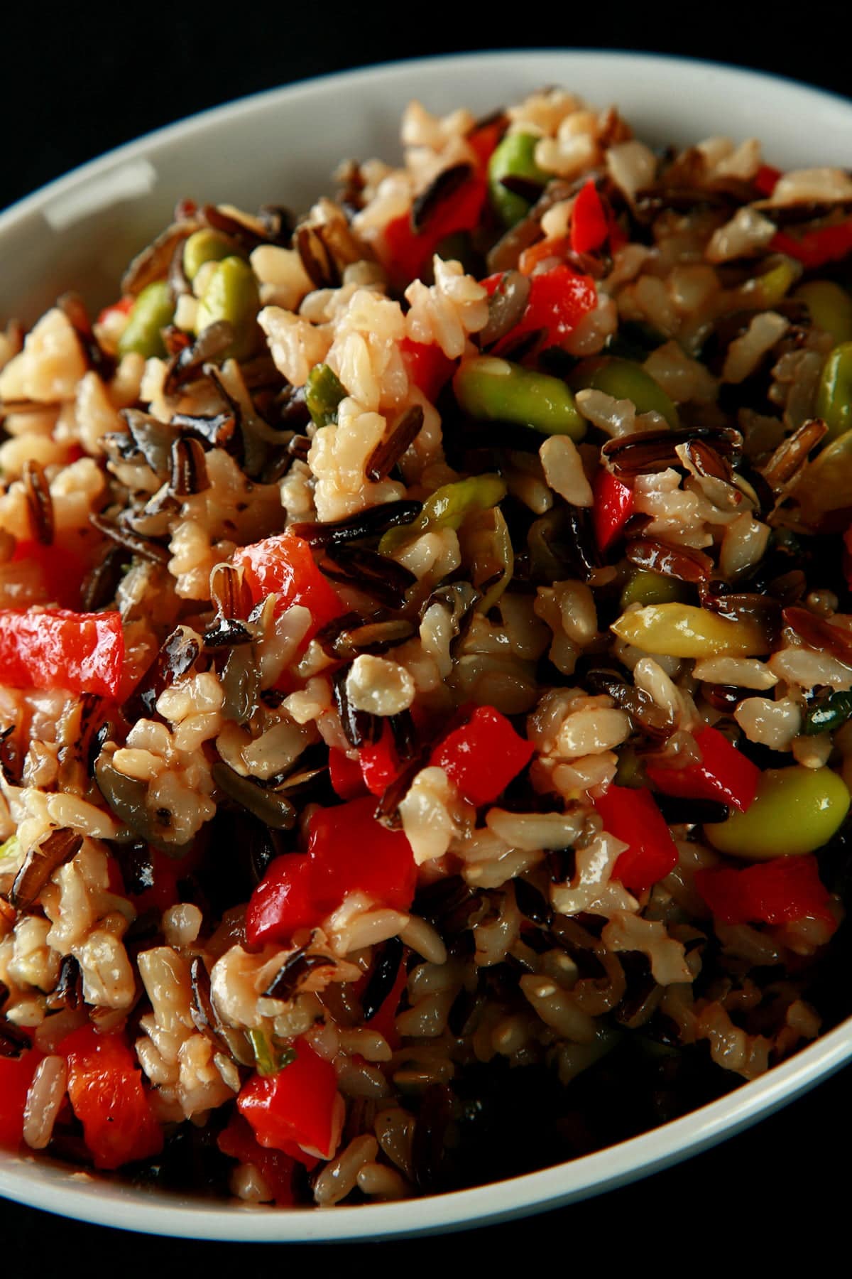A bowl of edamame wild rice salad.  Wild rice, edamame, and red peppers are all visible.