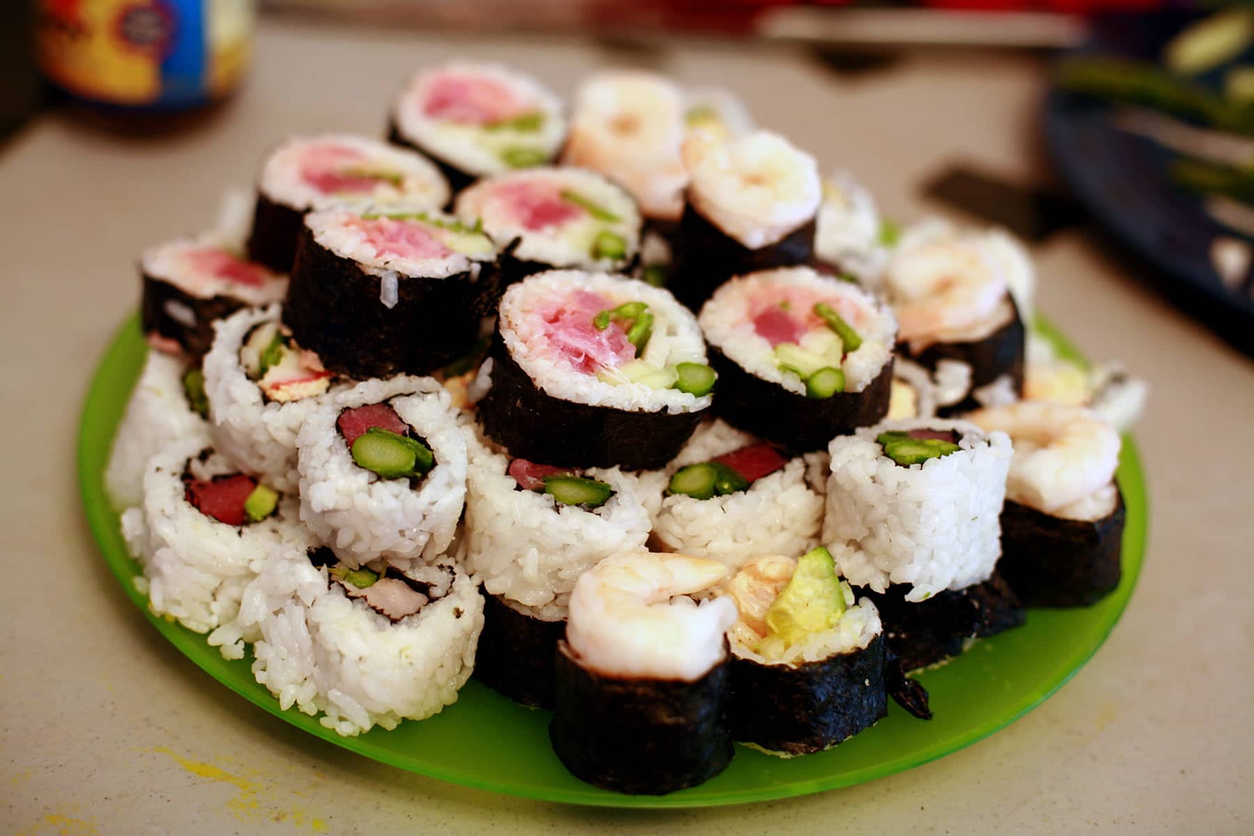 A large green plate is piled high with several different varieties of sushi roll slices.