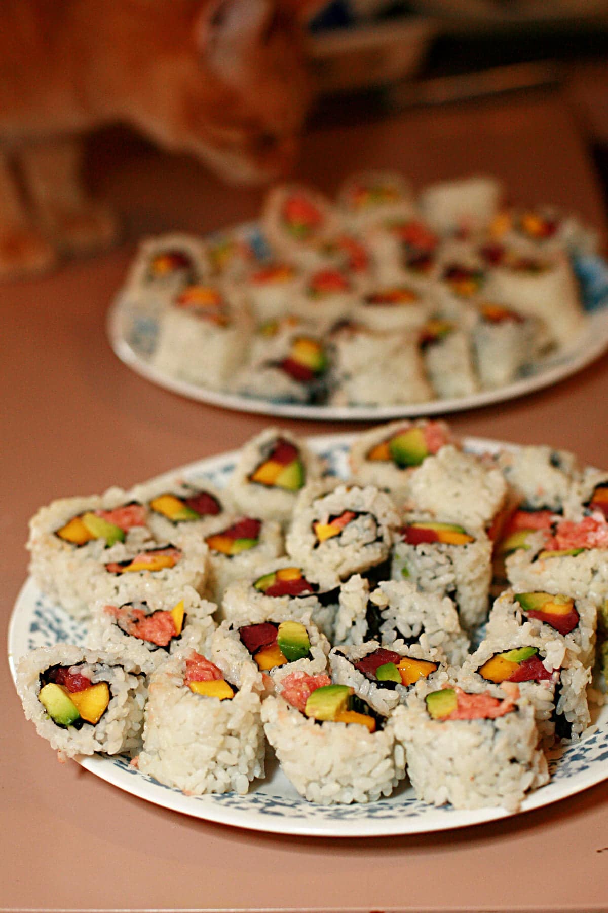 Two plates with dozens of pieces of DIY  sushi are shown on a pink countertop.