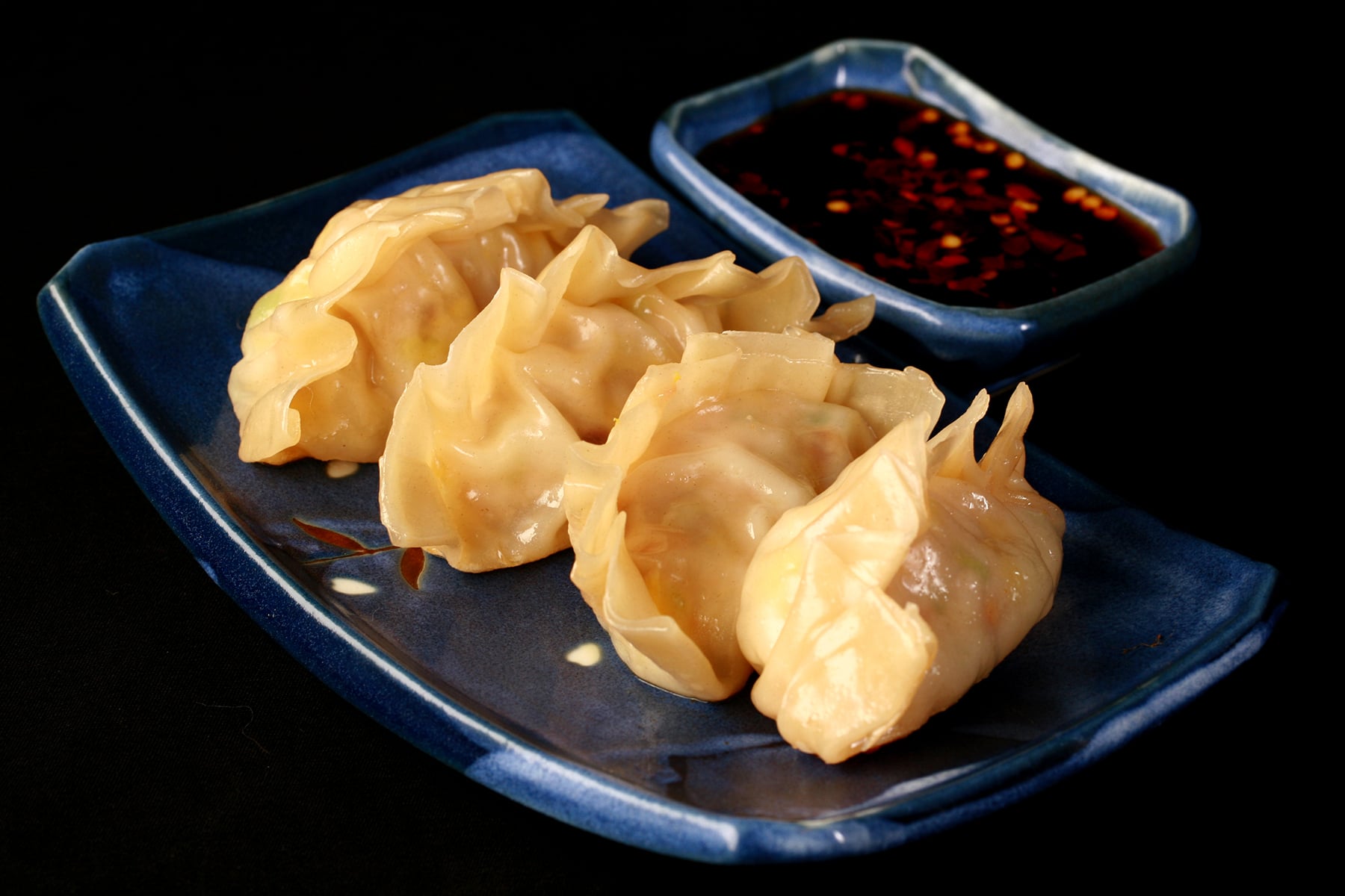 4 homemade potstickers on a blue rectangular plate, with a small dish of pot sticker sauce next to it.