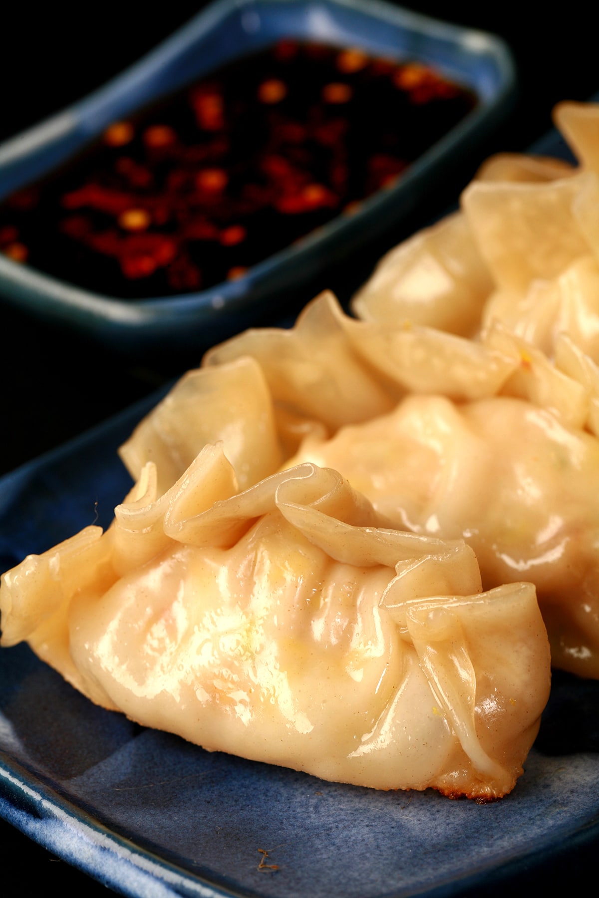 4 homemade gyoza on a blue rectangular plate, with a small dish of gyoza sauce next to it.