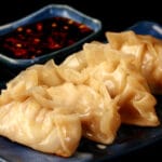 4 homemade potstickers on a blue rectangular plate, with a small dish of pot sticker sauce next to it.