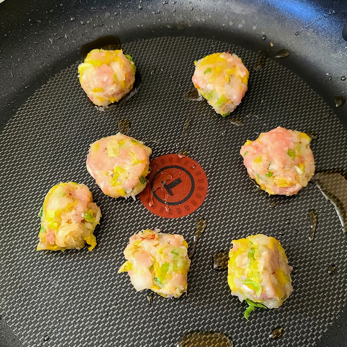 Balls of gyoza filling are cooking in a nonstick fry pan, meatball style.