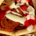 Close up view of a vegetarian donair - a pita bread folded around a pile of vegan donair "meat" slices, chopped red peppers, and donair sauce drizzled on top.