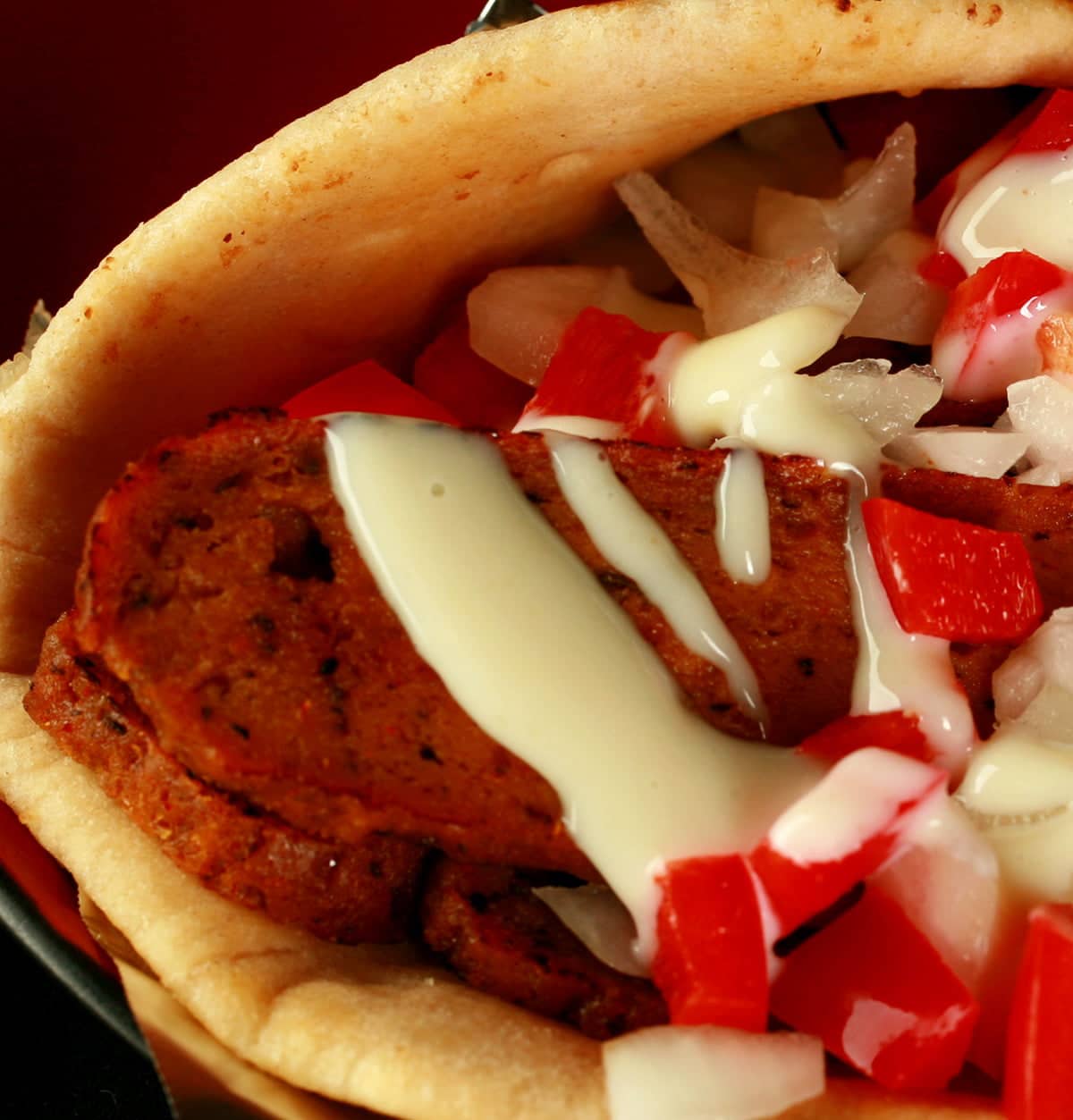 Close up view of a vegetarian donair - a pita bread folded around a pile of vegan donair "meat" slices, chopped red peppers, and donair sauce drizzled on top.