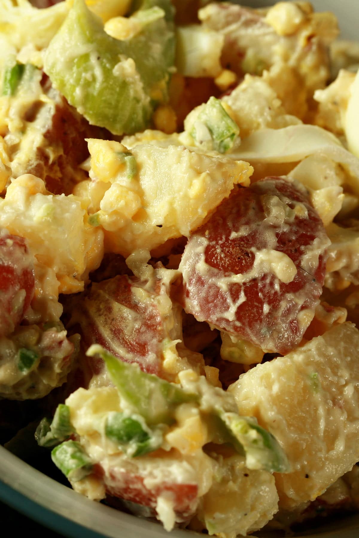 A bowl of a creamy cold-smoked potato salad. Chunks of red potatoes, celery slices, and hard boiled egg are all visible.