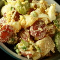 A bowl of a creamy smoked potato salad. Chunks of red potatos, celery slices, and hard boiled egg are all visible.