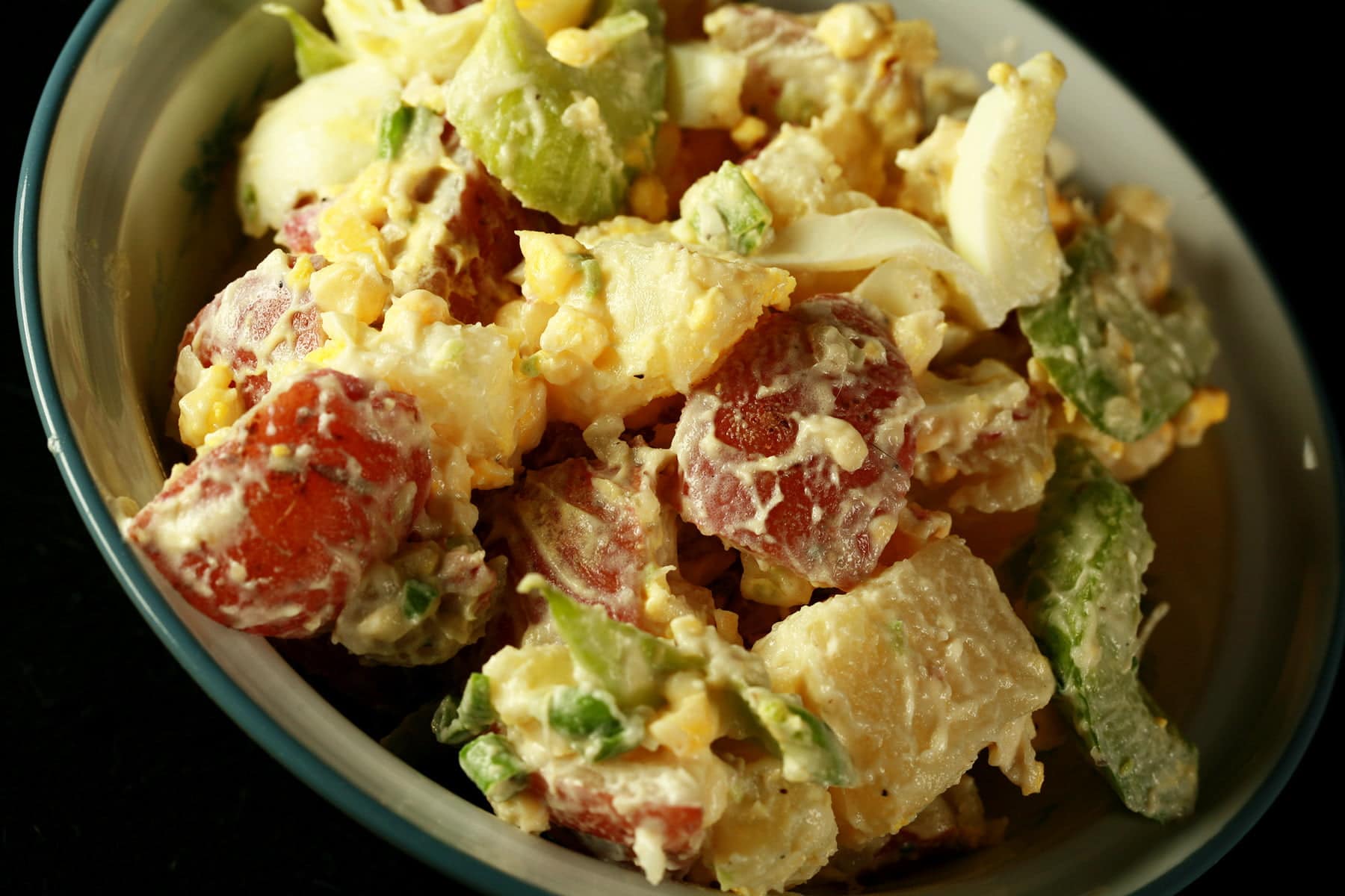 A bowl of a creamy smoked potato salad. Chunks of red potatoes, celery slices, and hard boiled egg are all visible.