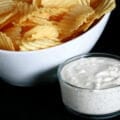 A large bowl of ripple chips is pictured next to a bowl of Dill Pickle Cream Cheese Dip.