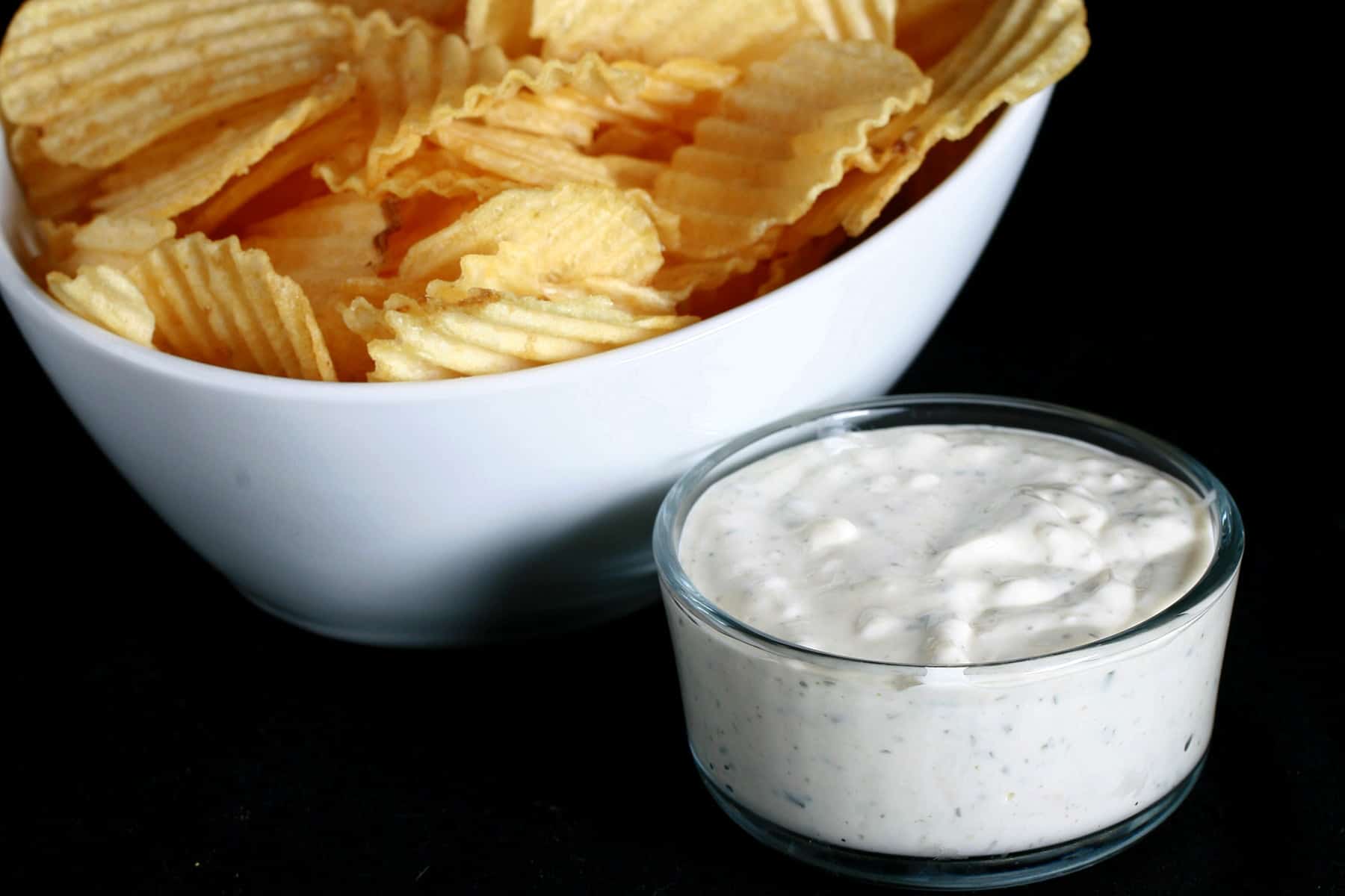 A large bowl of ripple chips is pictured next to a bowl of Dill Pickle Cream Cheese Dip.