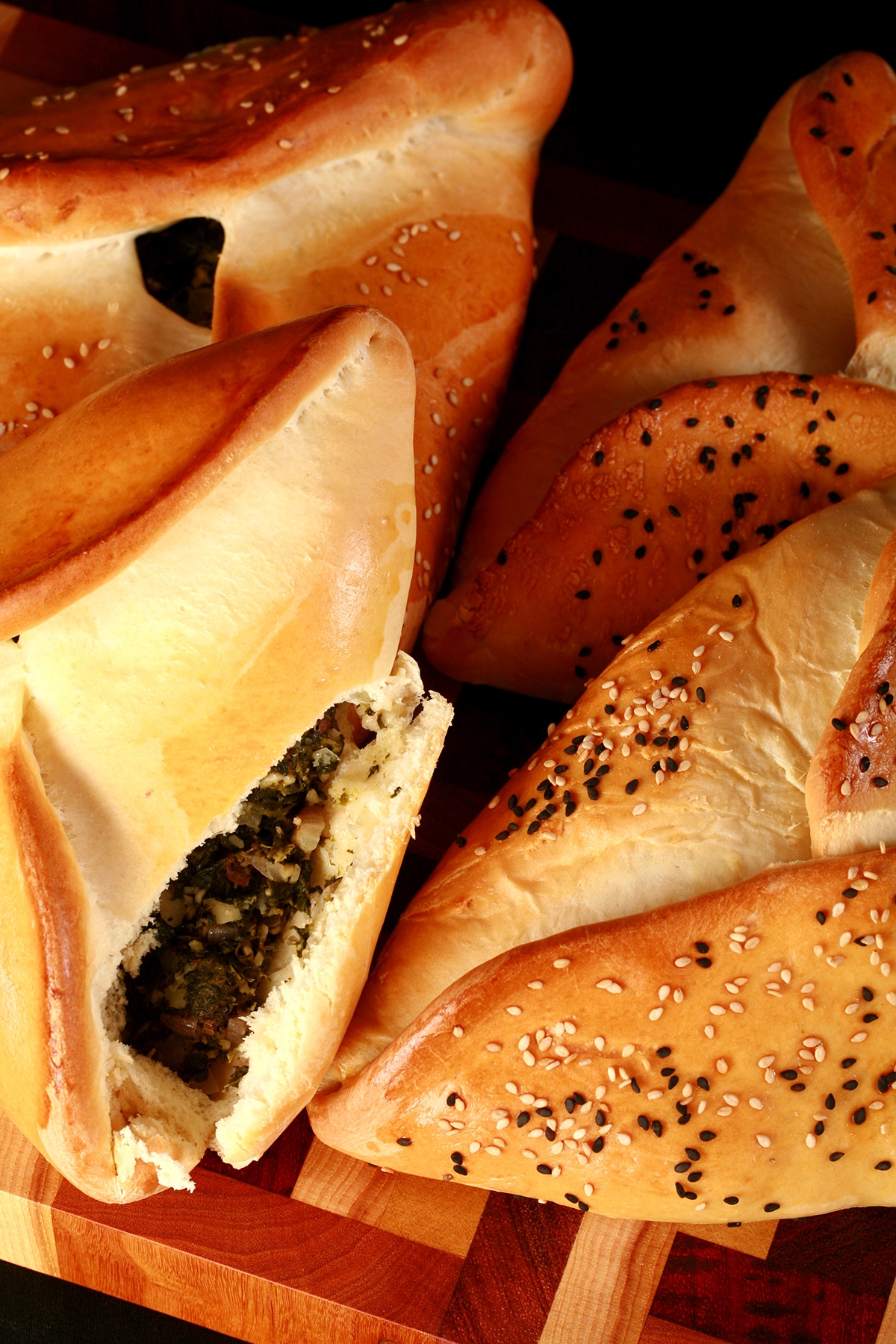 Close up view of 4 bread based spinach hand pies, covered with sesame seeds. One is opened, revealing the spinach and feta filling.