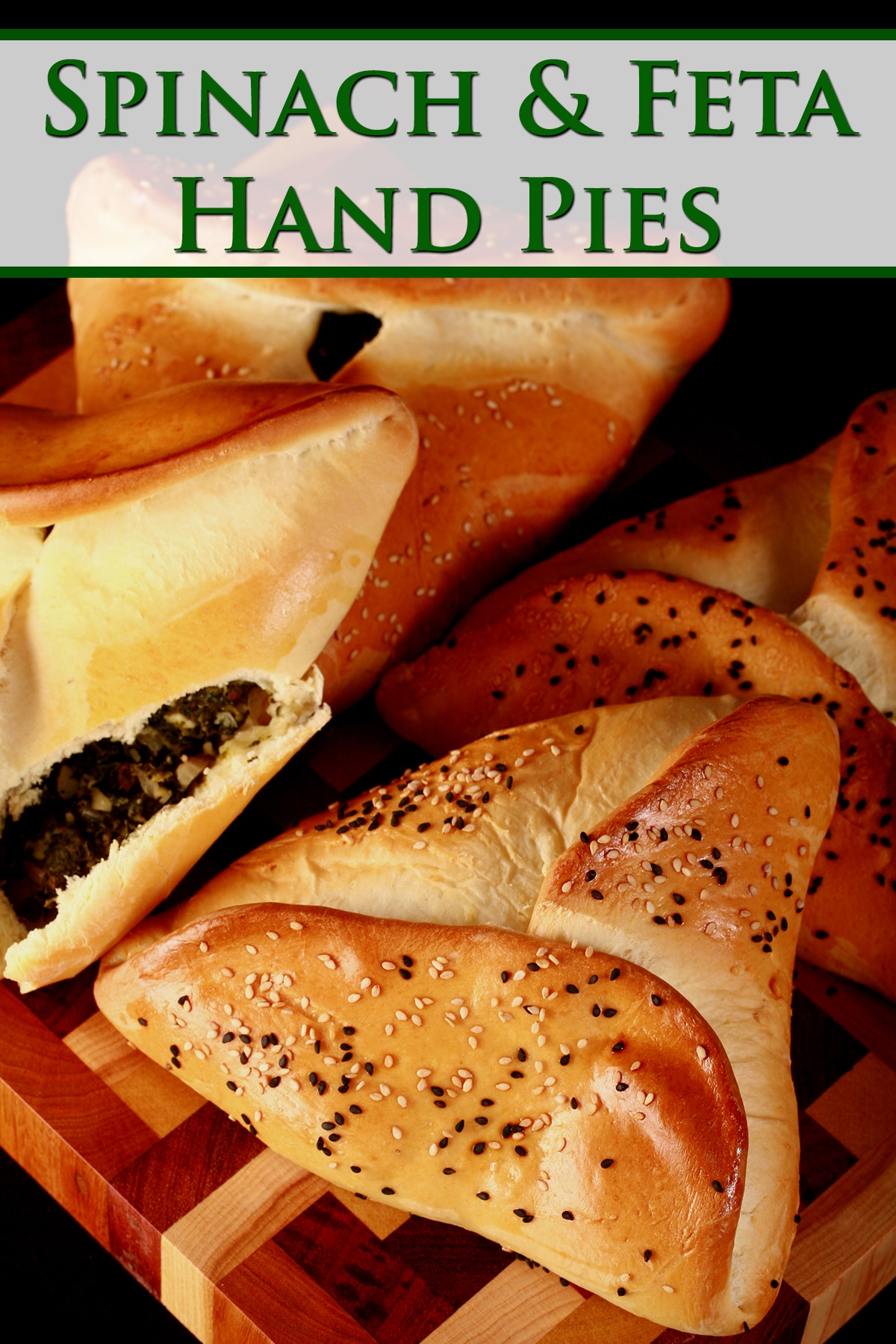 Close up view of 4 bread based spinach hand pies, covered with sesame seeds. One is opened, revealing the spinach and feta filling.