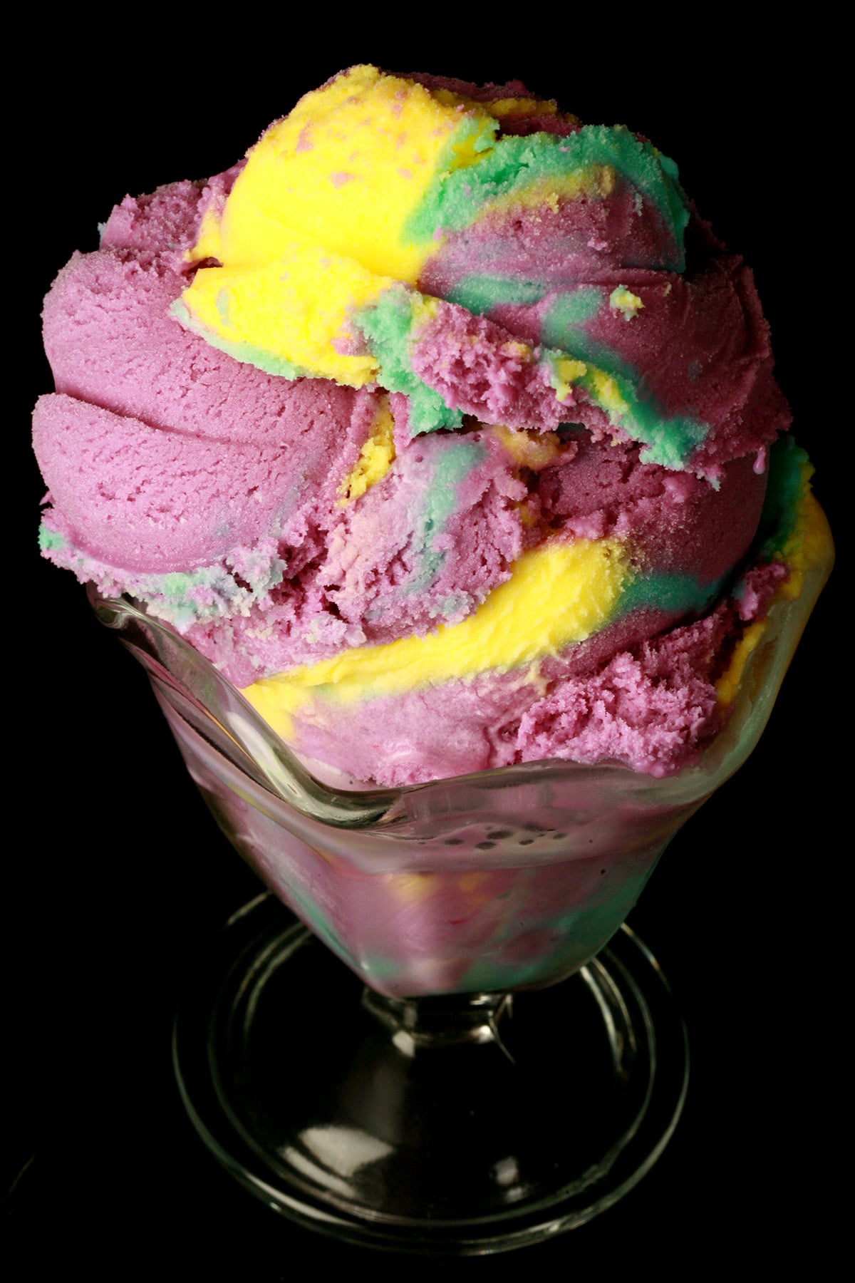 A fluted glass dessert bowl is stacked high with scoops of homemade moon mist ice cream - purple, blue, and yellow marbled ice cream.