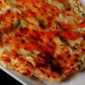 A close up view of a homemade crab rangoon pizza: Pizza crust, a cream cheese, green onion, and crab mixture, cheese, more green onions, and sweet thai chili sauce!
